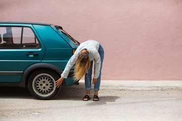 Female driver check tyre on her car. Pink wall background