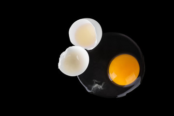 Broken white raw egg, yellow round yolk, two cracked halves of eggshell on black background isolated close up top view, unusual design, abstract concept, Easter banner, creative art poster, copy space