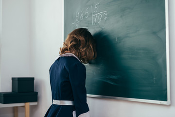 Wall Mural - Schoolgirl stands with her forehead on the chalkboard