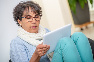 Wall Mural - charming senior brunette woman with glasses using digital tablet at home