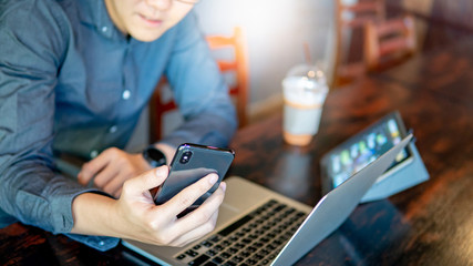 Wall Mural - Male hand holding smartphone. Businessman using laptop computer and digital tablet while working in the cafe. Mobile app or internet of things concepts. Modern lifestyle in digital age.