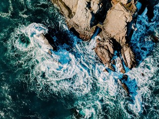 Wall Mural - Aerial view of ocean waves and rocks. Blue  sea surface.