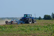 Blue tractor plowing the green field with an iron harrow in the plowing season