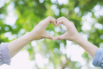 Wall Mural - Young couple lover show holding hands make heart shape over in public parks.	