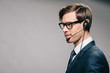 handsome man in suit and glasses wearing headset on grey background