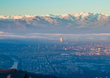 Fototapeta Miasto - Panoramic view at sunrise on Turin city seen from Superga in winter, with a layer of smog that falls on buildings, snowy Alps mountains on background
