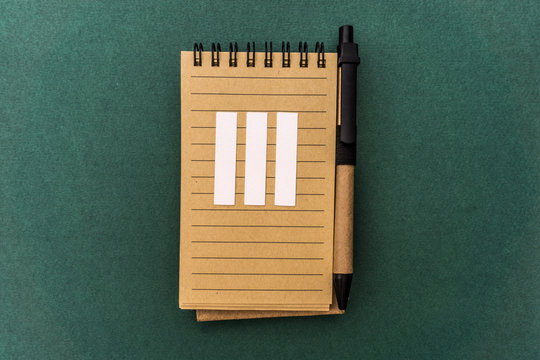 Notebook front with pen and white three Roman number on green background. Spiral notepad on a table. Three, 3 chapter, March.