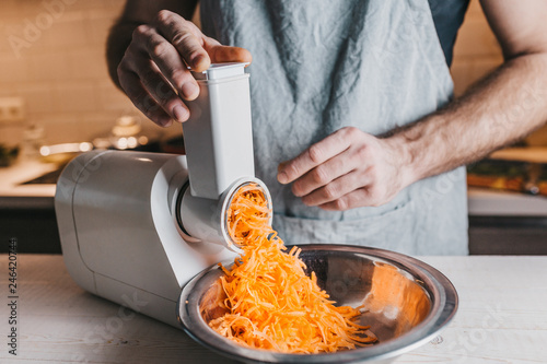 Photographie Closeup of a rough male chef hands chopping carrots on an electric meat grinder