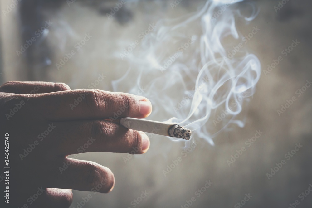 man holding smoking a cigarette in hand. Cigarette smoke spread. dark  background Stock Photo