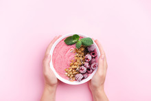 Woman's hands holding raspberries smoothie bowl with mint leaf on pink background. Top view, copy space.