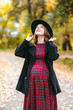 © sushytska - Beautiful autumn girl in the park. Lots of yellow leaves. Girl in a gray coat and red dress. Pregnant girl holding hands belly