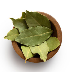 dried bay leaves in a dark wood bowl isolated on white from above.