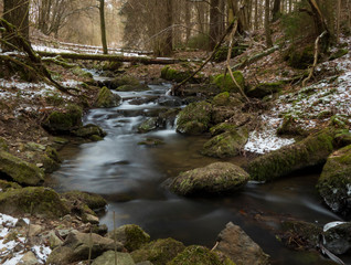 smooth motion of wild water in a river in winter with snow and ice on rocks and stones in the beautiful nature of a forest