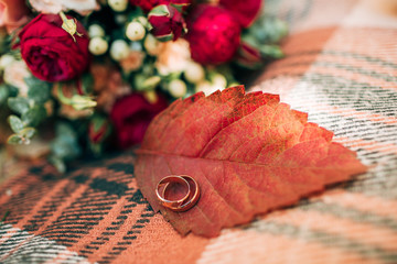 Wedding rings on autumn leaf. Beautiful wedding bouquet of red and beige roses.