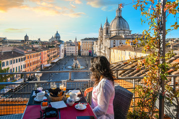 A woman enjoys the view of Rome, Italy and the Piazza Navona as she finishes her continental breakfast from a rooftop terrace of a luxury hotel early on a summer morning.