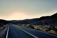 Paved Desert Road Leading Into Horizon At Sunset