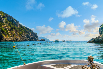 A small boat heads towards other boats and out of the Palaiokastritsa  bay towards the Aegean Sea on the Island of Corfu Greece.