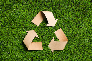 Recycling symbol cut out of kraft paper on green grass, top view