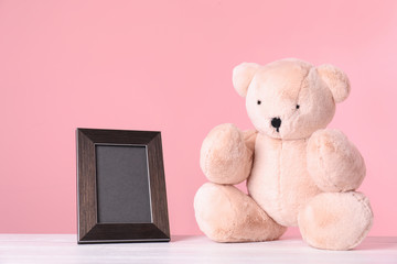 Photo frame with space for text and adorable teddy bear on table against color background. Child room elements