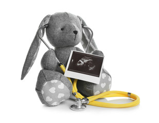 Ultrasound photo of baby and toy rabbit on white background. Concept of pregnancy