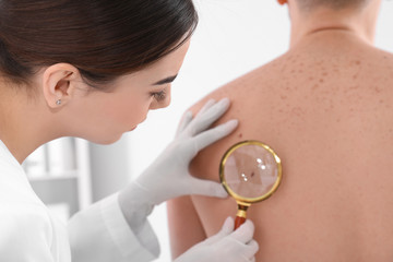 Dermatologist examining patient with magnifying glass in clinic, closeup view