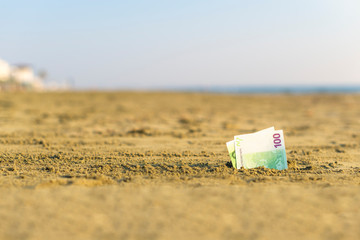 Banknote of value of one hundred euro in the the sand on the beach. Concept of cheap travel and vacation. Promotion and discount