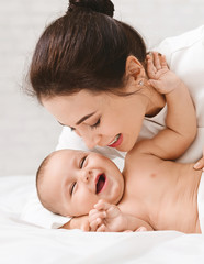 Wall Mural - Mother tickling her baby playing in bed at home