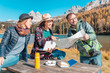 © EdNurg - A group of friends with a map and a laptop in a mountain reserve on the shore of a beautiful lake are looking for a good hotel to book on the Internet to continue the adventure