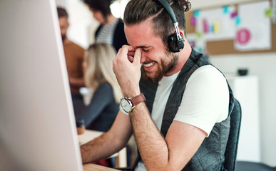 Wall Mural - Young businessman with headphones and colleagues in a modern office.