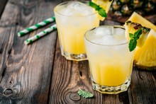 Fresh Pineapple Juice In Two Glasses With Ice And Mint On Dark Rustic Background