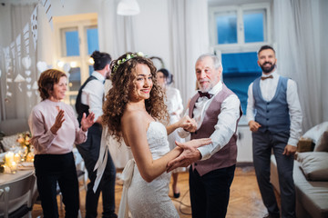 Wall Mural - A young bride dancing with grandfather and other guests on a wedding reception.