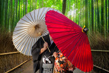 Fototapeta Bambus - Couple with traditional japanese umbrellas posing at bamboo forest in Arashiyama