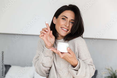 Photographie Image of smiling woman 30s holding jar with face cream, in modern bright room