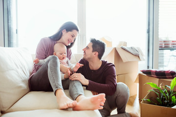 A portrait of young couple with a baby and cardboard boxes moving in a new home.