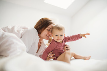 a young mother with little daughter sitting indoors on bed in the morning, playing.