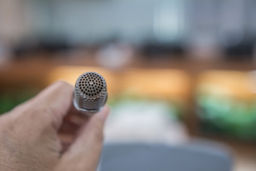 Speaker holding microphone for speaking, presentation on stage in public conference seminar hall with light background. Business meeting and education in teaching classroom concept