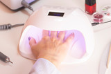Fototapeta  - The hands of the girl in the UV lamp for nails on the manicure table