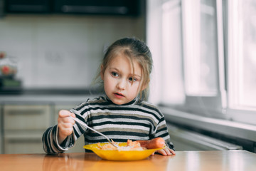 Wall Mural - girl eating pasta with sausage in the kitchen in a striped jacket