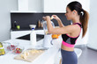 © nenetus - Sporty young woman preparing strawberry and banana smoothie with blender in the kitchen at home.