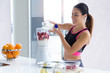 © nenetus - Sporty young woman preparing strawberry and banana smoothie with blender in the kitchen at home.