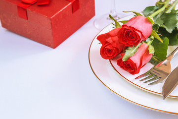 Wall Mural - Festive table setting with bouquet of red roses and gift box on white plate with copy space