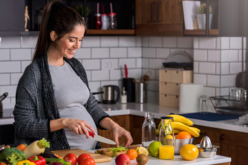 beautiful smiling young pregnant woman preparing healthy food with lots of fruit and vegetables at h