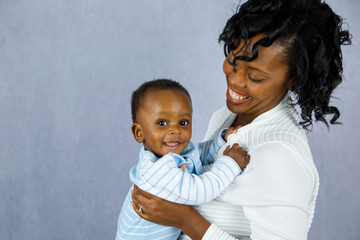 Wall Mural - Beautiful African Amercian Woman wHolding Her Baby boy on a Gray Background