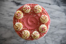 Close Up Of Pink Frosted Cake With White Swirls And Heart Shaped Sprinkles