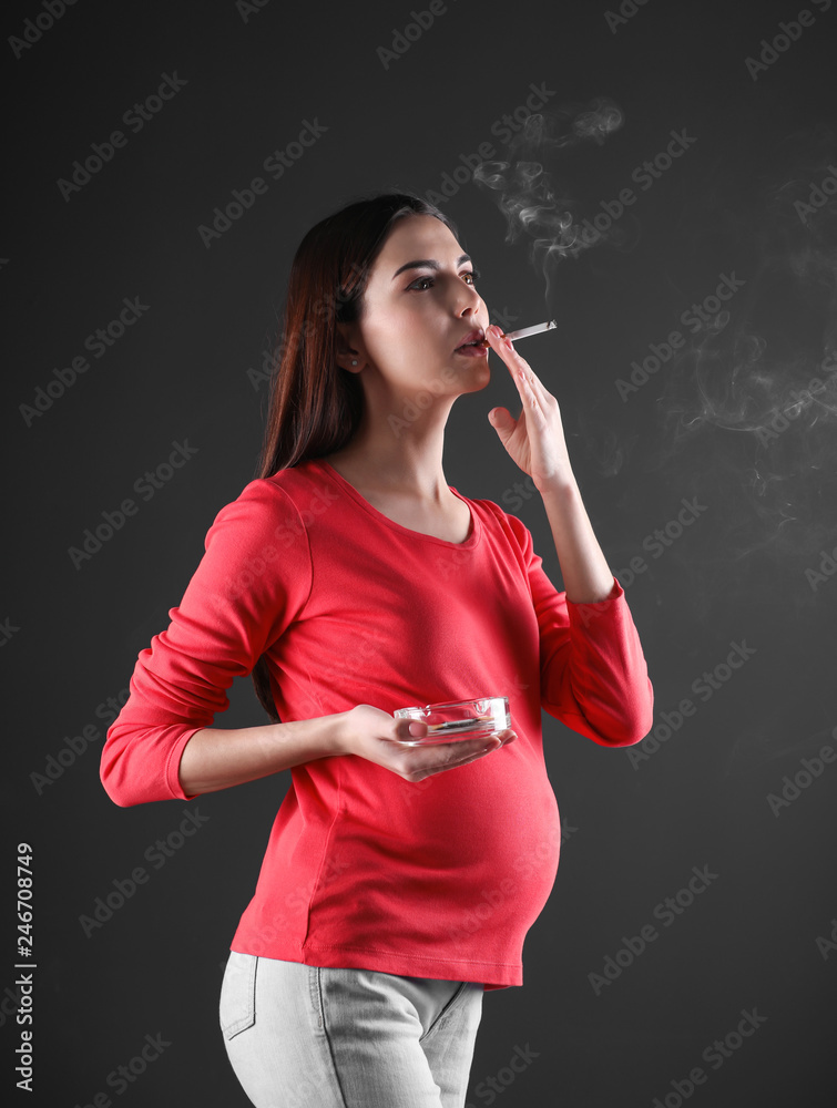 Pregnant woman smoking cigarette on black background Stock Photo