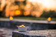 Macro shot of lit candle burning with soft glowing flame and smoke on romantic sunset background. Candle path at the park close to the seaside during the Night of ancient lights