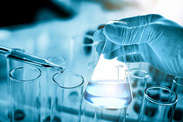 hand of scientist holding flask with lab glassware in chemical laboratory background, science laboratory research and development concept 