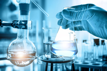 hand of scientist holding flask with lab glassware in chemical laboratory background, science labora