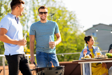 Wall Mural - leisure and people concept - happy friends with bbq grill and non-alcoholic drinks having barbecue party on rooftop in summer