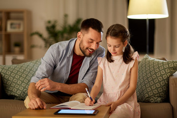 Wall Mural - education and family concept - happy father and daughter with book and tablet computer doing homework together at home in evening